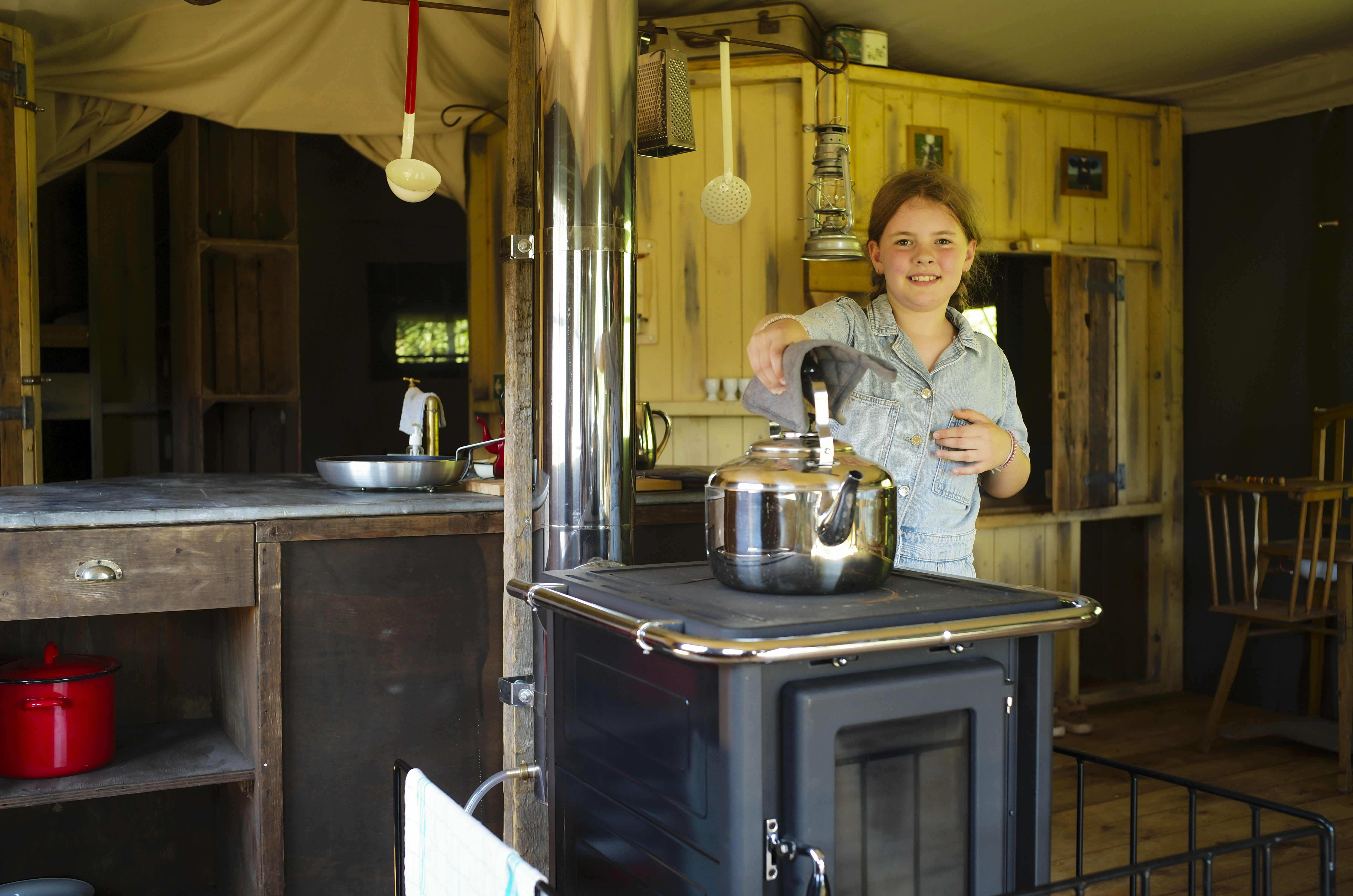 Petite fille qui soulève une théière au-dessus du poêle à bois dans le lodge